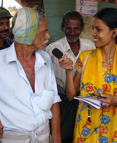 A woman reporter interviews an older man while another man looks on