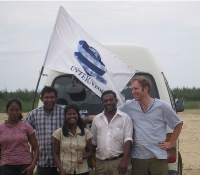 A group of 5 people stand by a van with an Internews flag