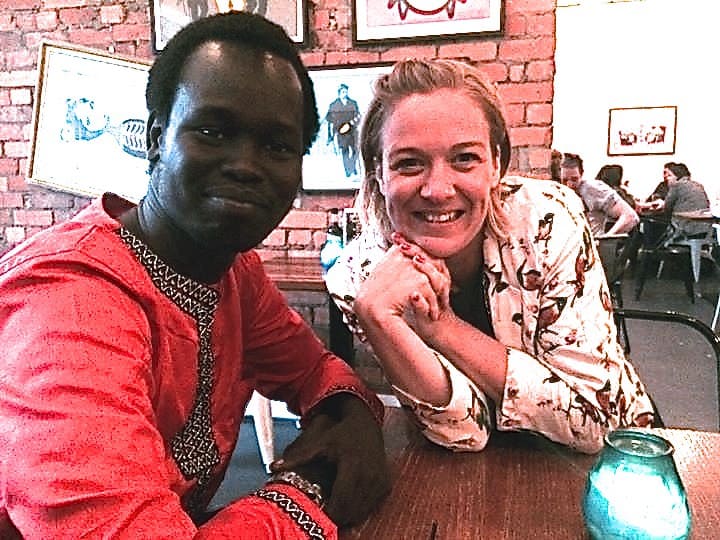 A man and woman sit at a table in a cafe smiling for the camera
