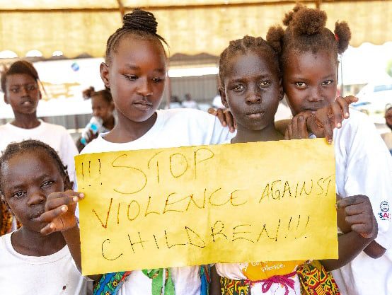 Four girls hold a poster that says: Stop Violence Against Children