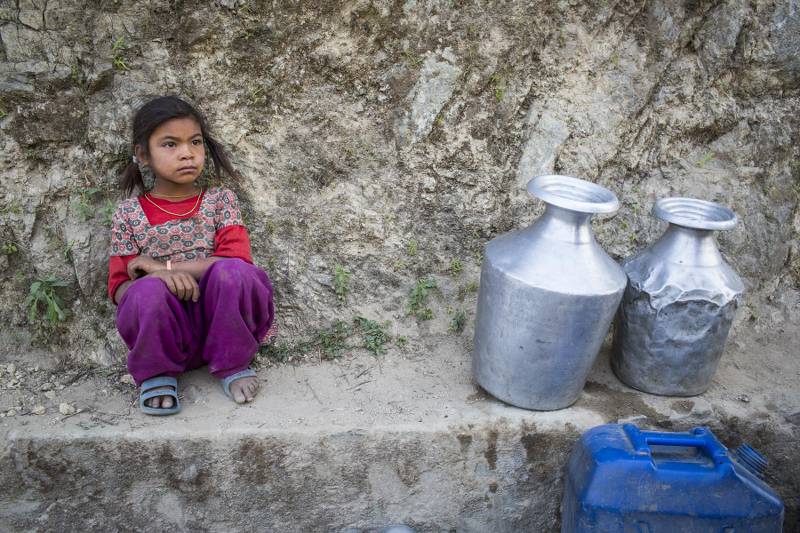 A young girl sits with 2 metal containers by a water source