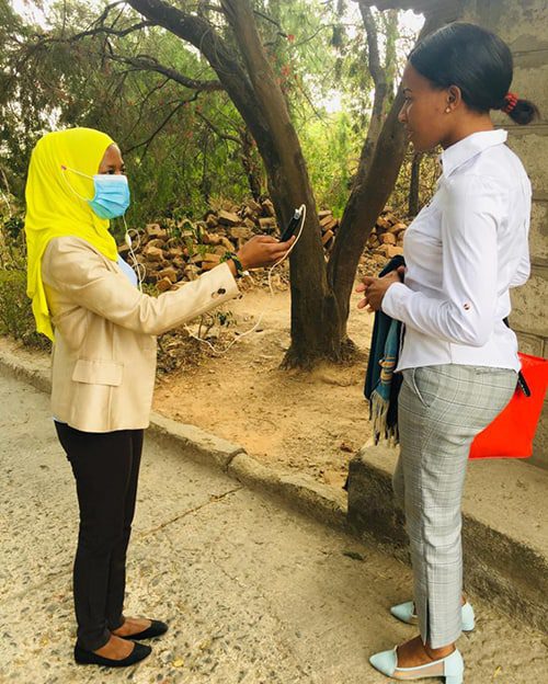 A woman wearing a mask holds a mic up to another woman, not wearing a mask