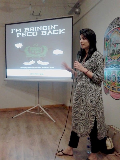 Farieha Aziz stands in front of a room speaking in a mic with a projector screen