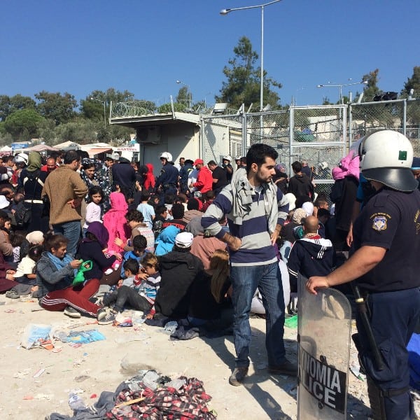 Refugees wait by a fenced area on the island