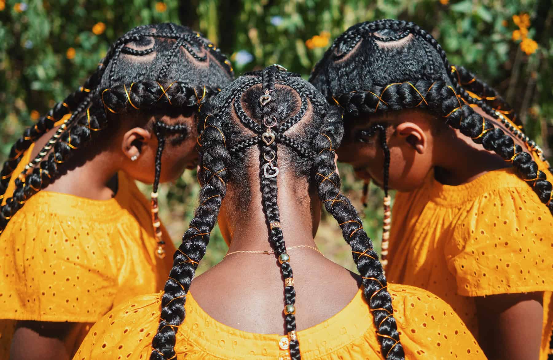 The top and back of 3 young Black women's heads are shown elaborately braided