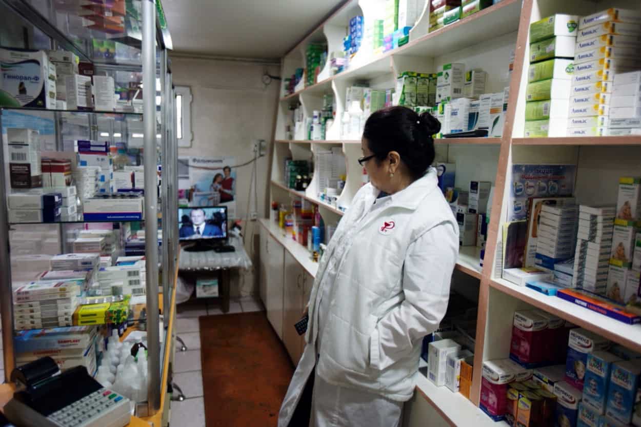 A woman in a white coat stands between two shelves of medications