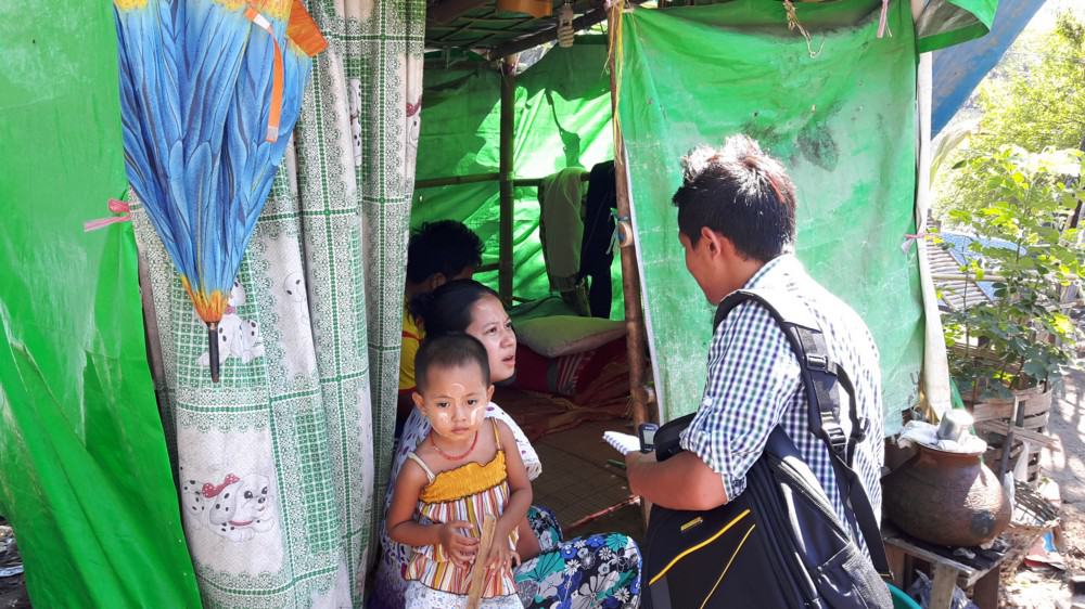 A journalist interviews a woman with a baby in a tent