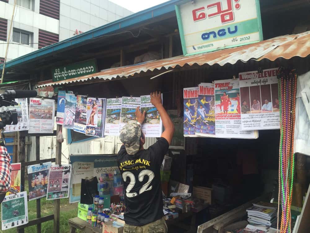 A man hangs a newspaper up at a newsstand