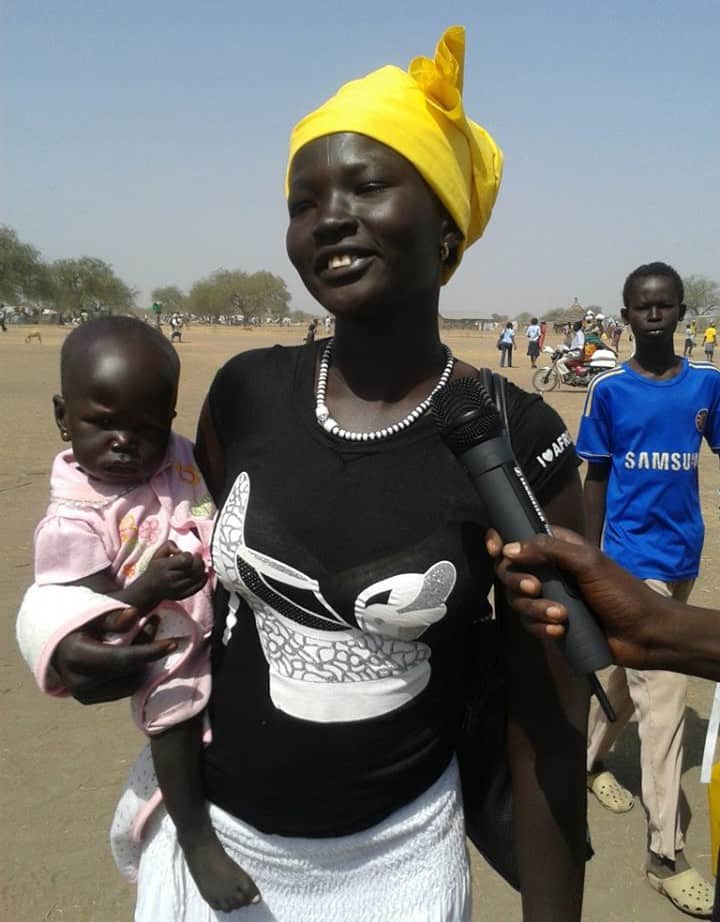 A woman stands outside in the heat holding her baby