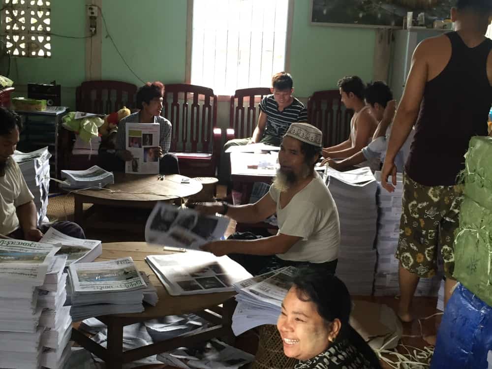 Staff sit in a room folding newspapers on tables