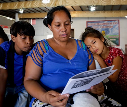 A girl rests her head on a woman's shoulder while the woman reads a newspaper