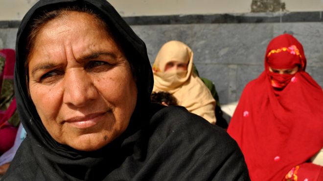 Closeup of an older woman wearing a black abaya; two women sit behind her.