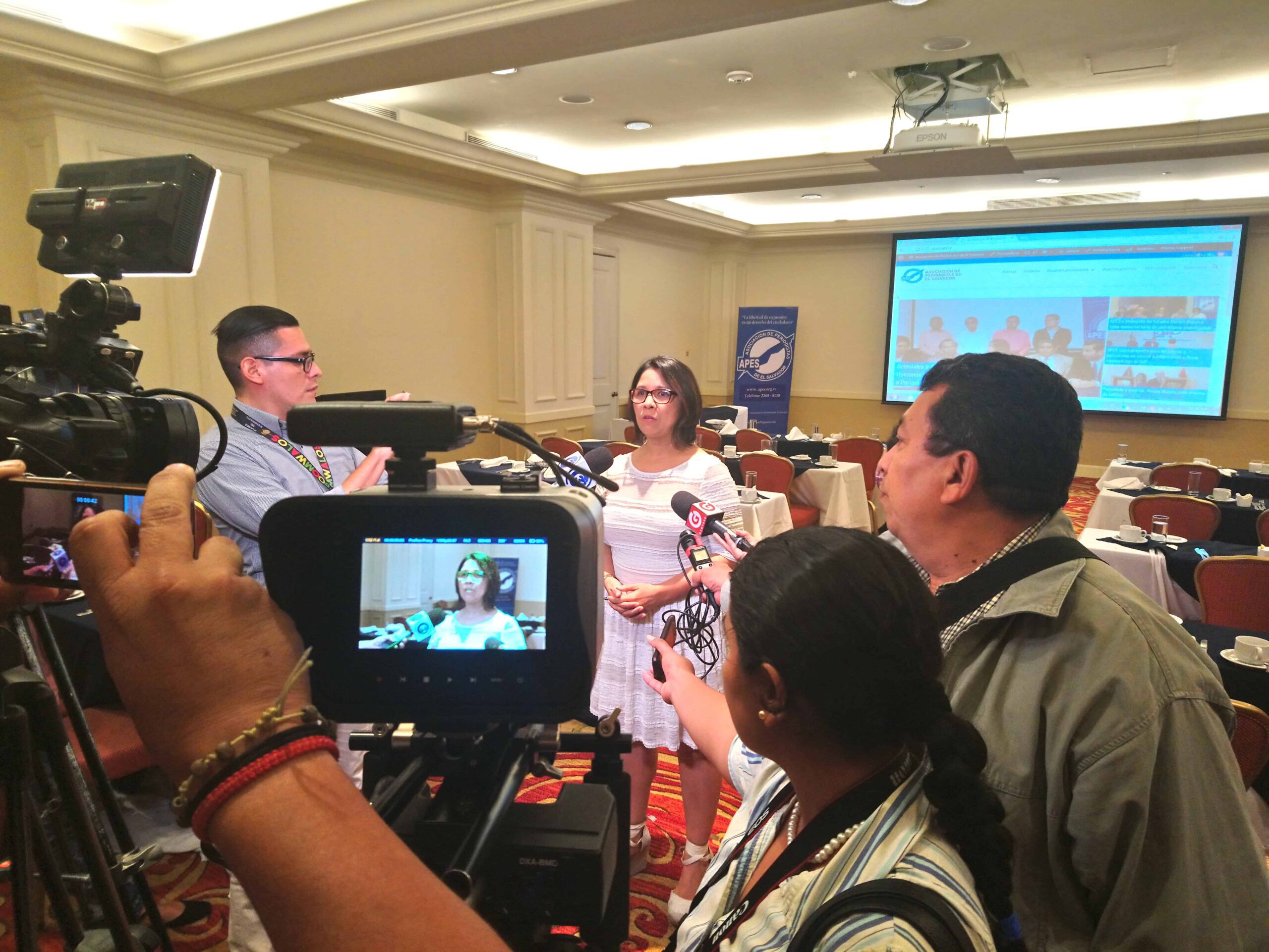 A group of journalists interviews a woman (Dalila Arriaza) using video cameras and microphones.