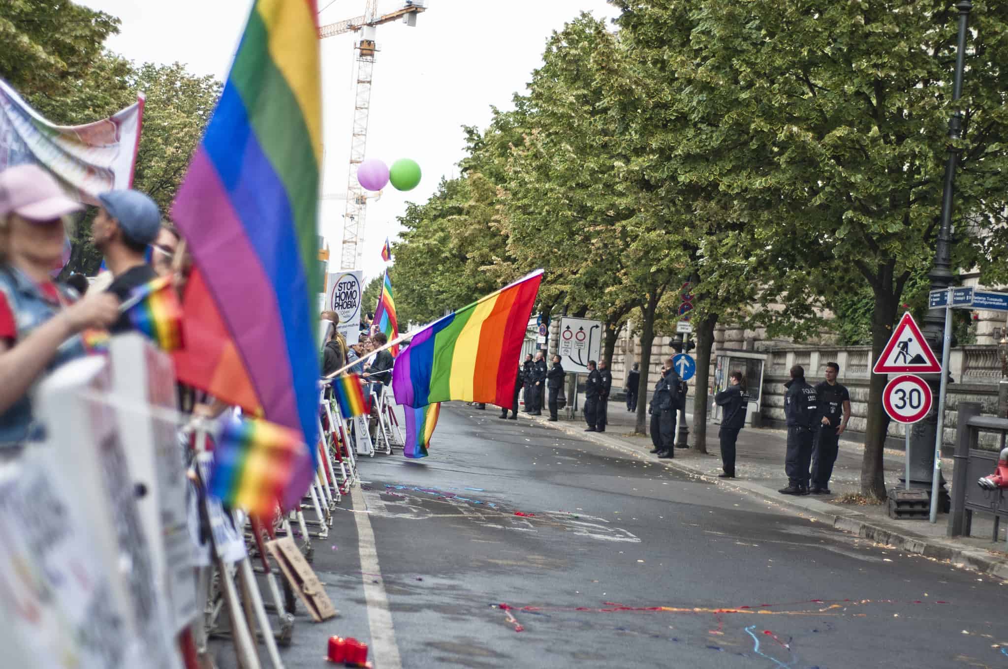 People holding rainbow flags line up on one side of the street; across the street is a line of police.