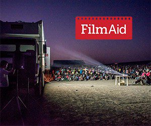 People sit outside watching a film on the side of a truck - FilmAid