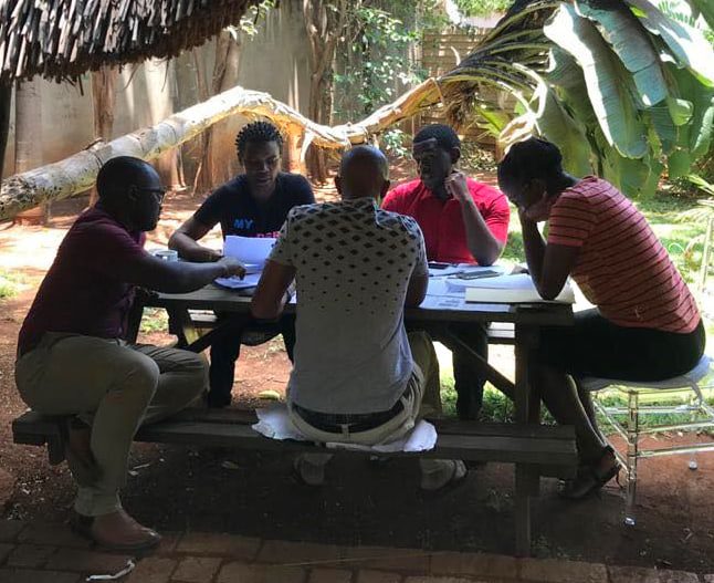 5 people sit outside around a picnic table looking at papers