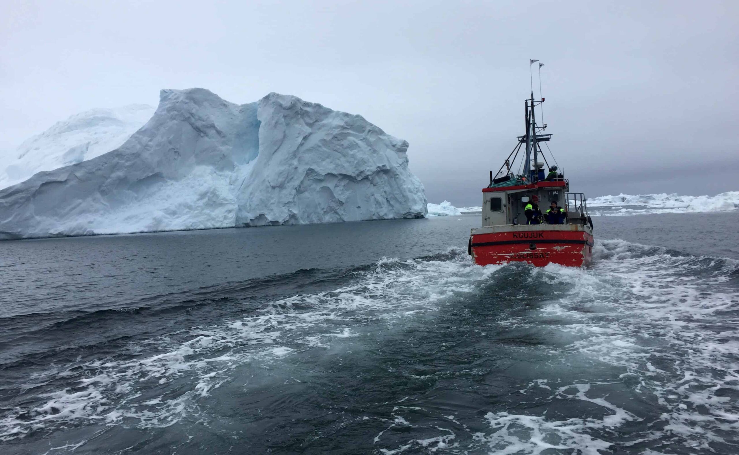 A fishing boat runs past an iceberg