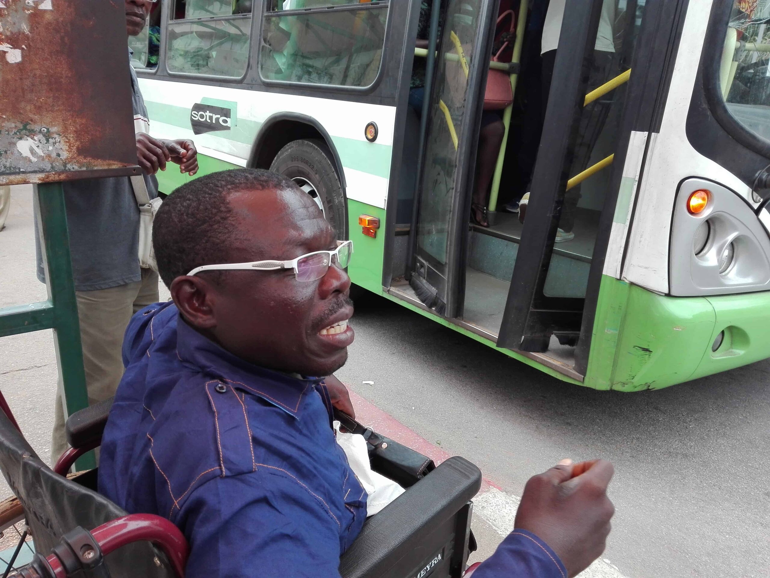 A man in a wheelchair waits on the side of the street where a bus has stopped.
