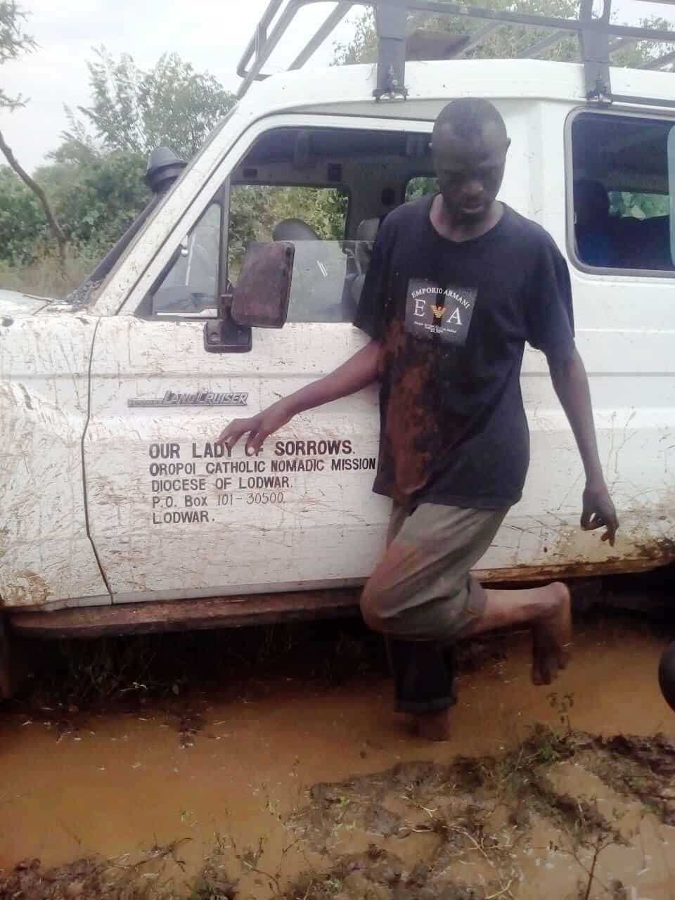 A man stands next to a truck that is stopped in muddy water