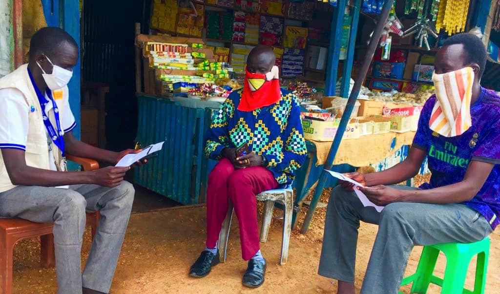 Three people sit in a circle in chairs at an outdoor market.