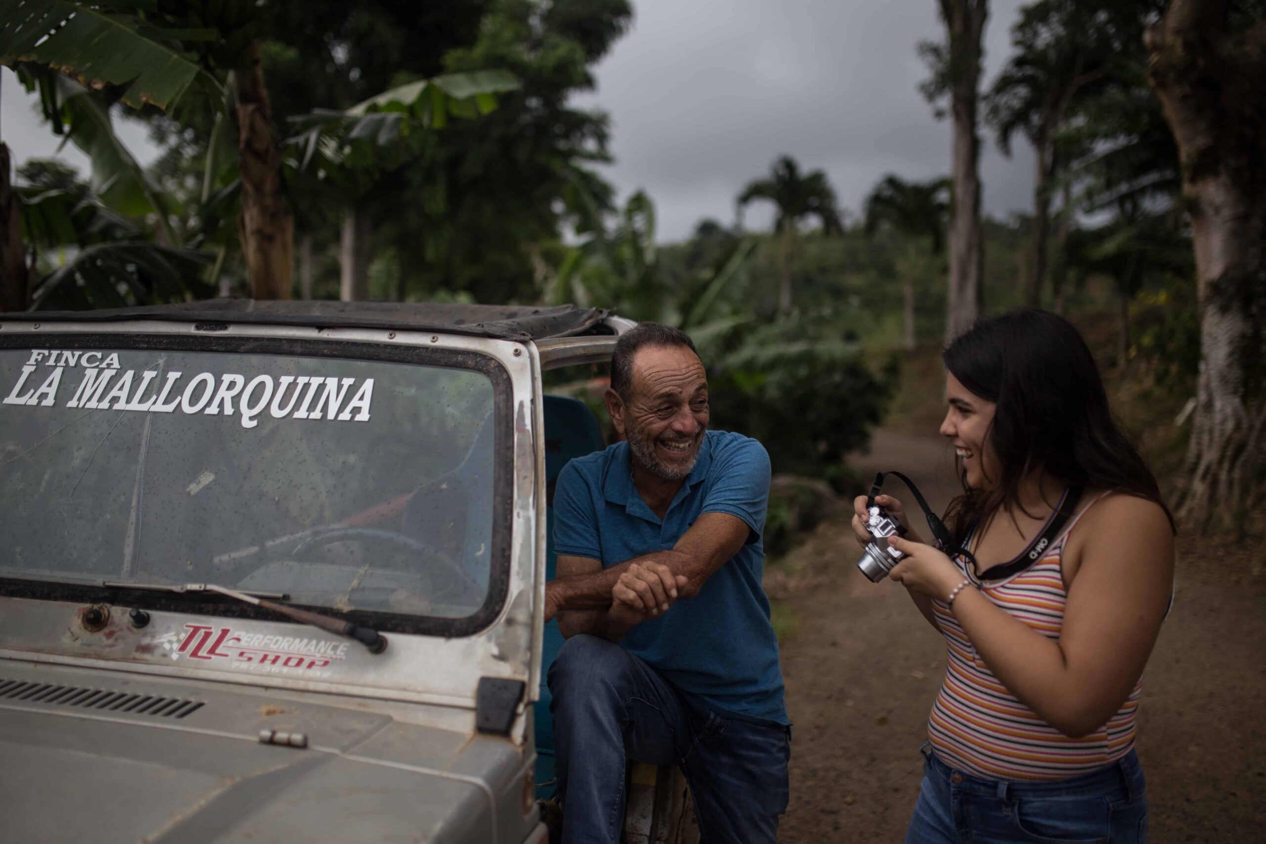 A young woman with a camera talks to a man who is standing beside a pickup truck.