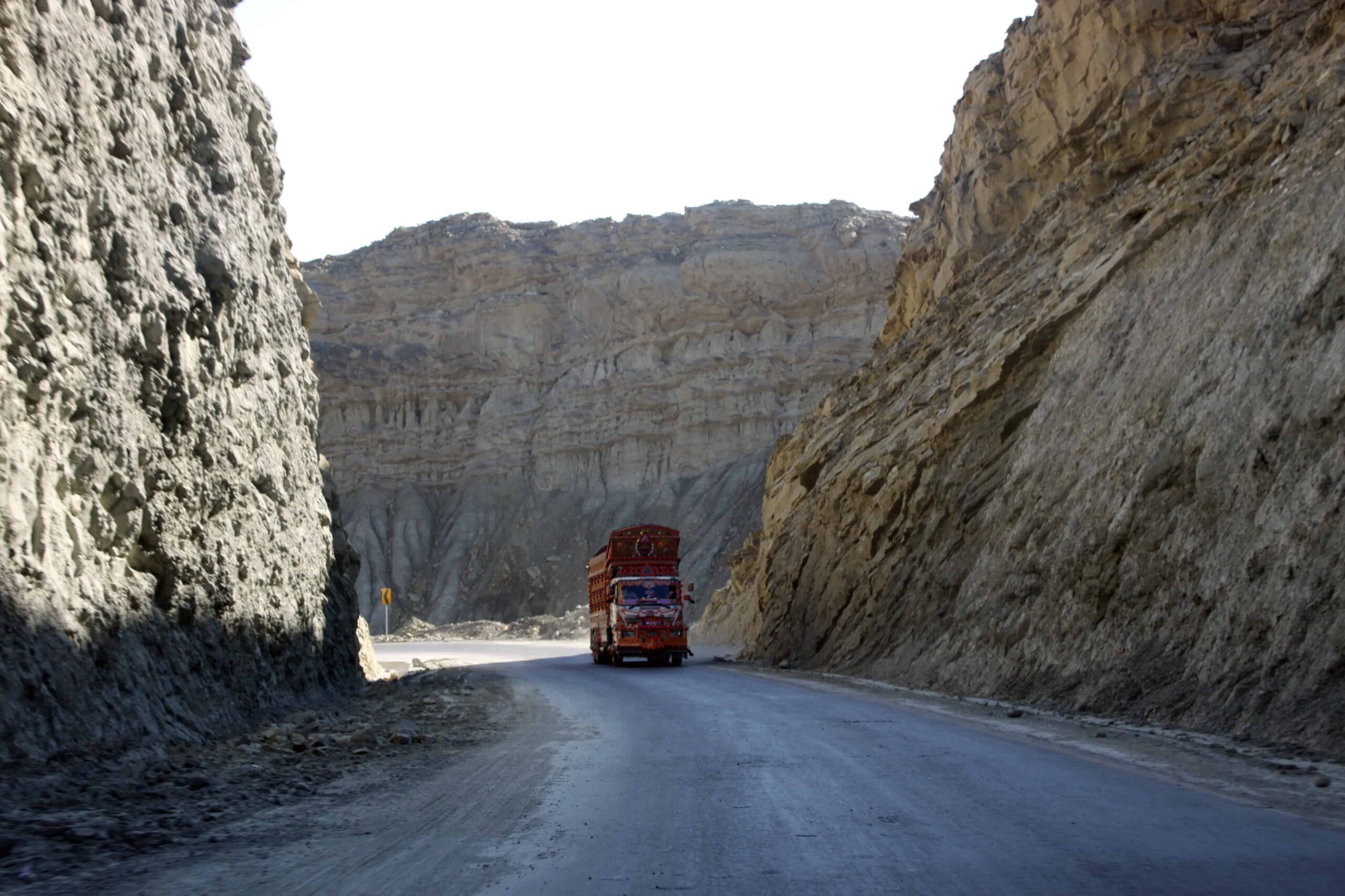 A truck travels on a highway with high cliffs on both sides.