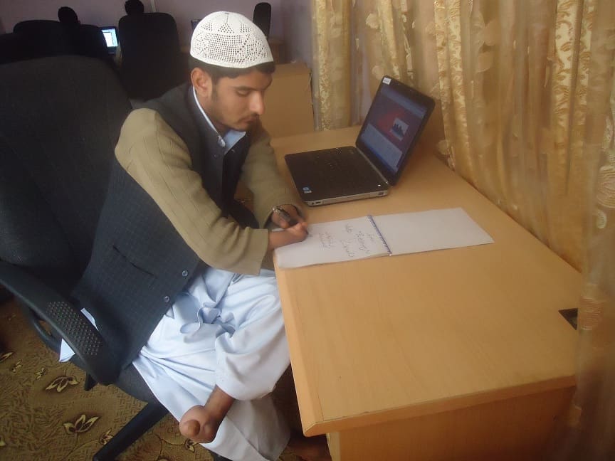 A man with a hand disability sits at a desk writing