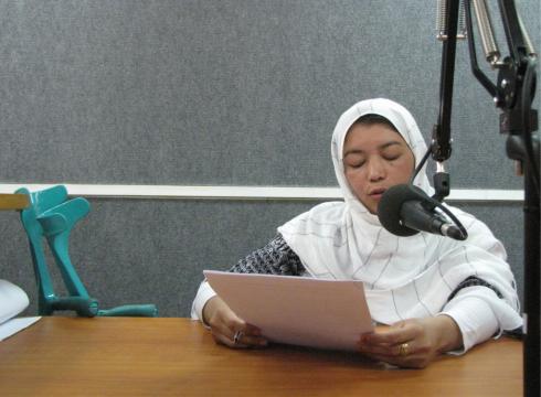 Amina sits at a microphone reading from a paper