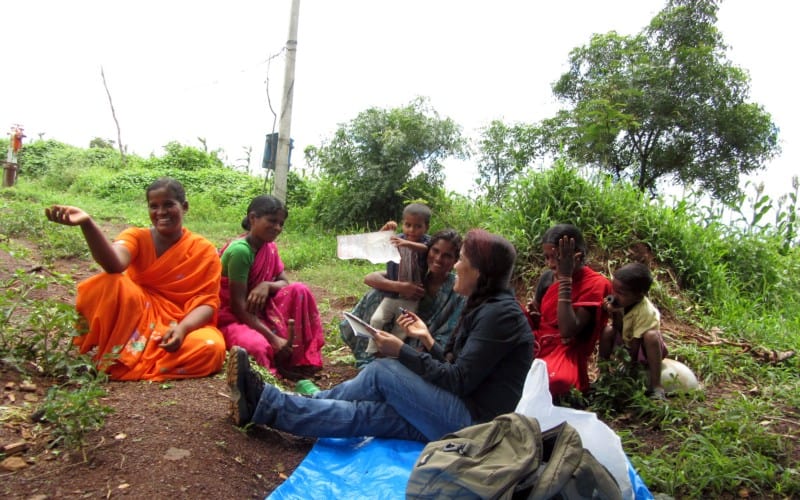 A group of women sit in the grass talking; most are wearing saris