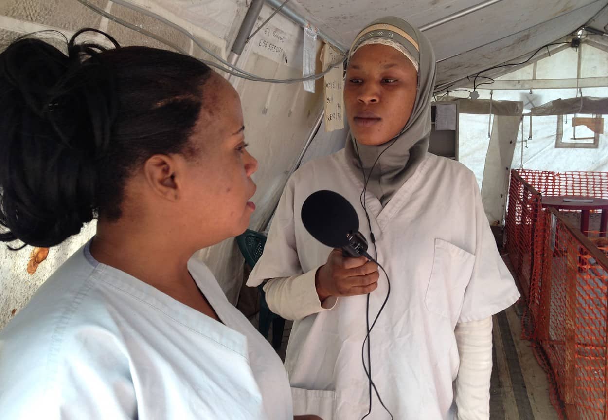A woman journalist interviews a health worker in a tent