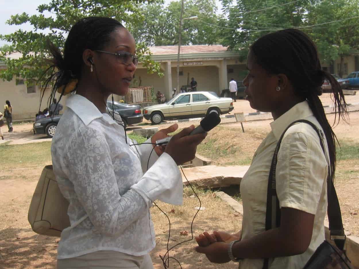 A woman journalist interviews another woman outside under a tree