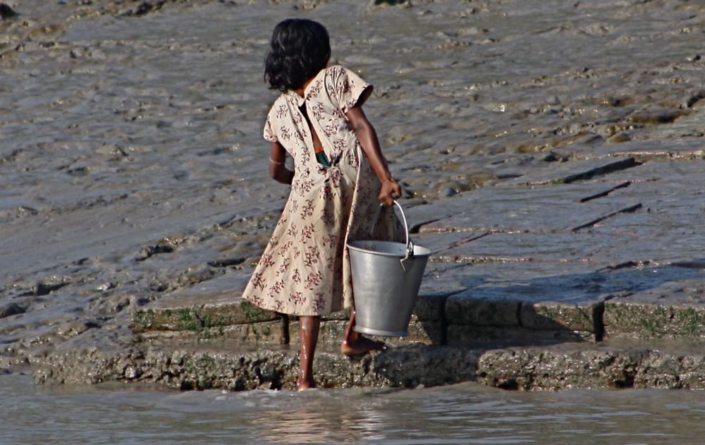 A young girl carries a bucket of water up the steps from the river