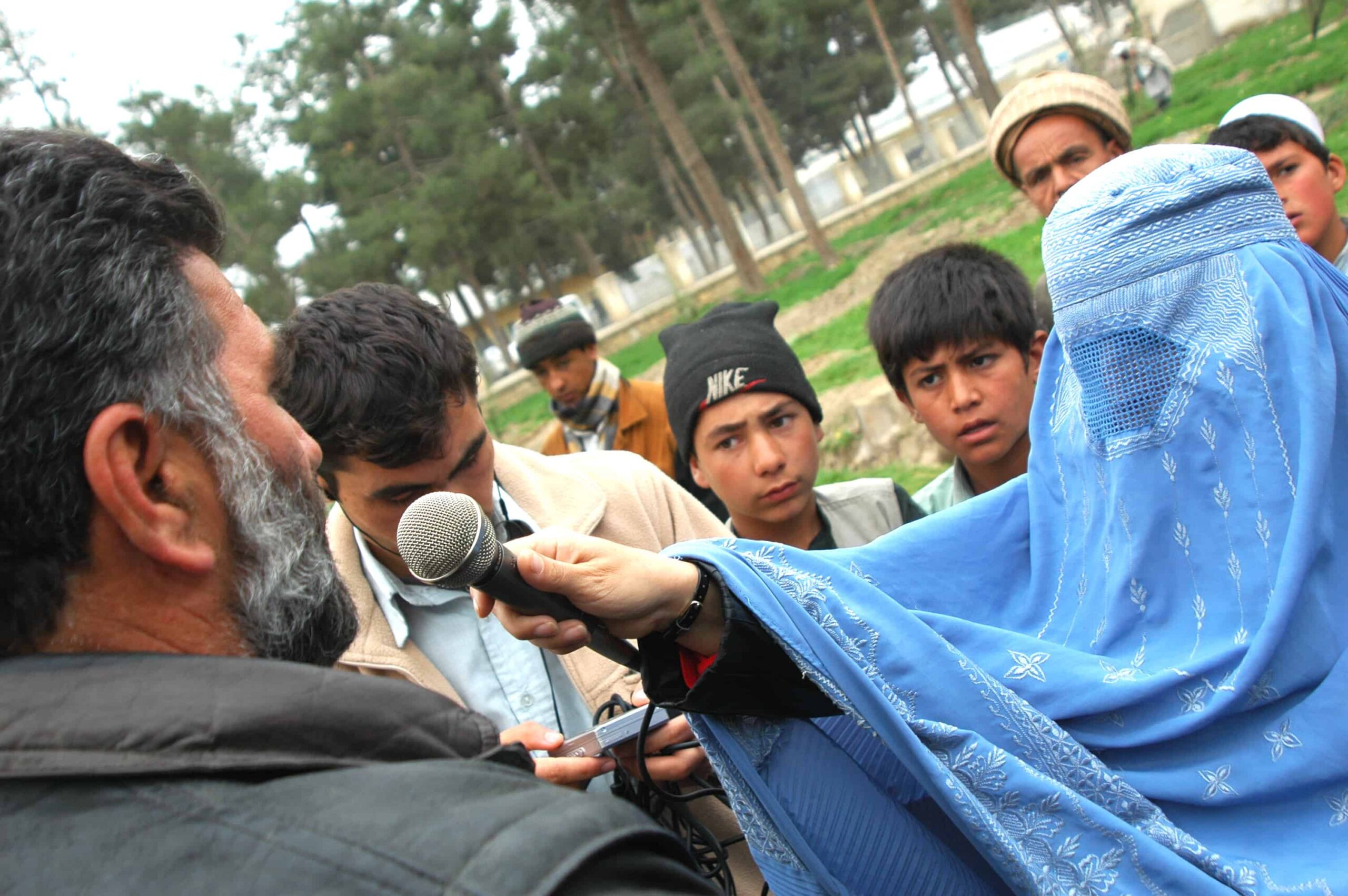 An Afghan woman in a burqa interviews some men