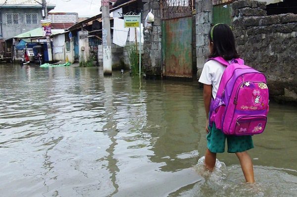 A girl carrying a pink backpack walks through ankle-deep water in a flooded street