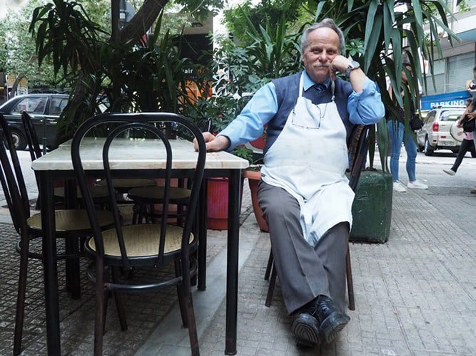 A man wearing a white apron sits at an outdoor table
