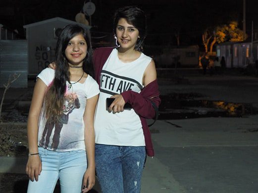 Two young women wearing t-shirts and jeans stand outside at night