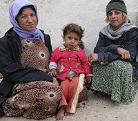 Two Iraqi women sit next to each other, one holds a child