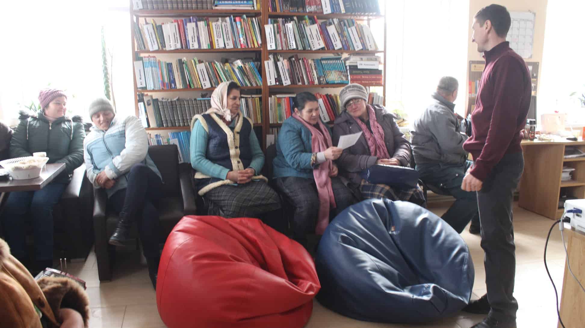 People sit in a library looking at printed material. A bookshelf is behind them.