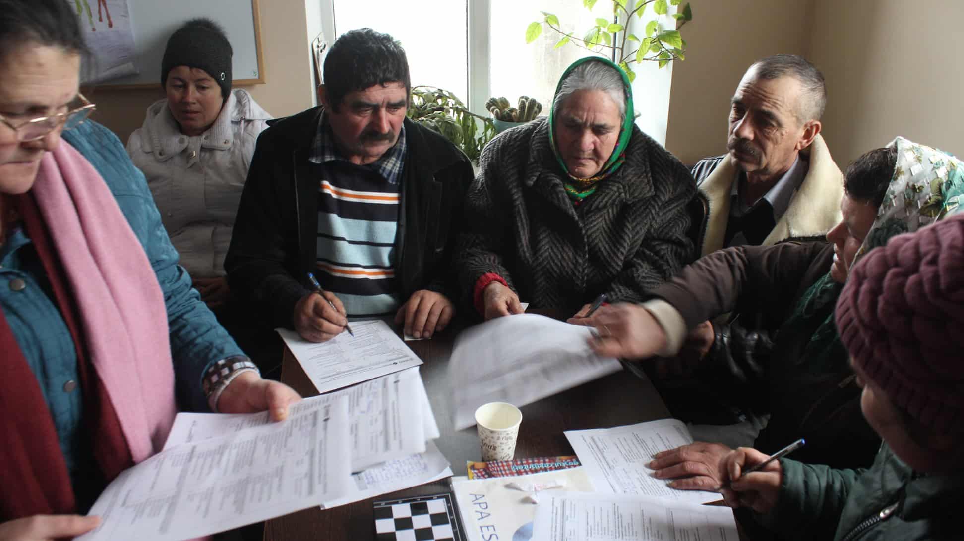 A group of older people sit around a table looking at printed material.