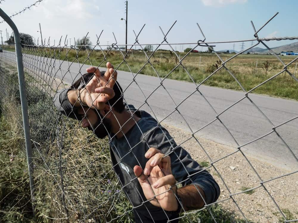 A man leans against a wire fence
