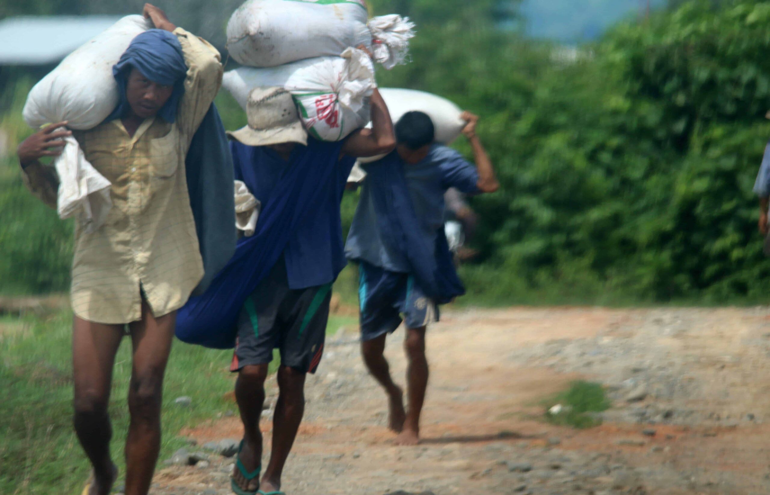 3 men carry heavy sacks down a dirt road