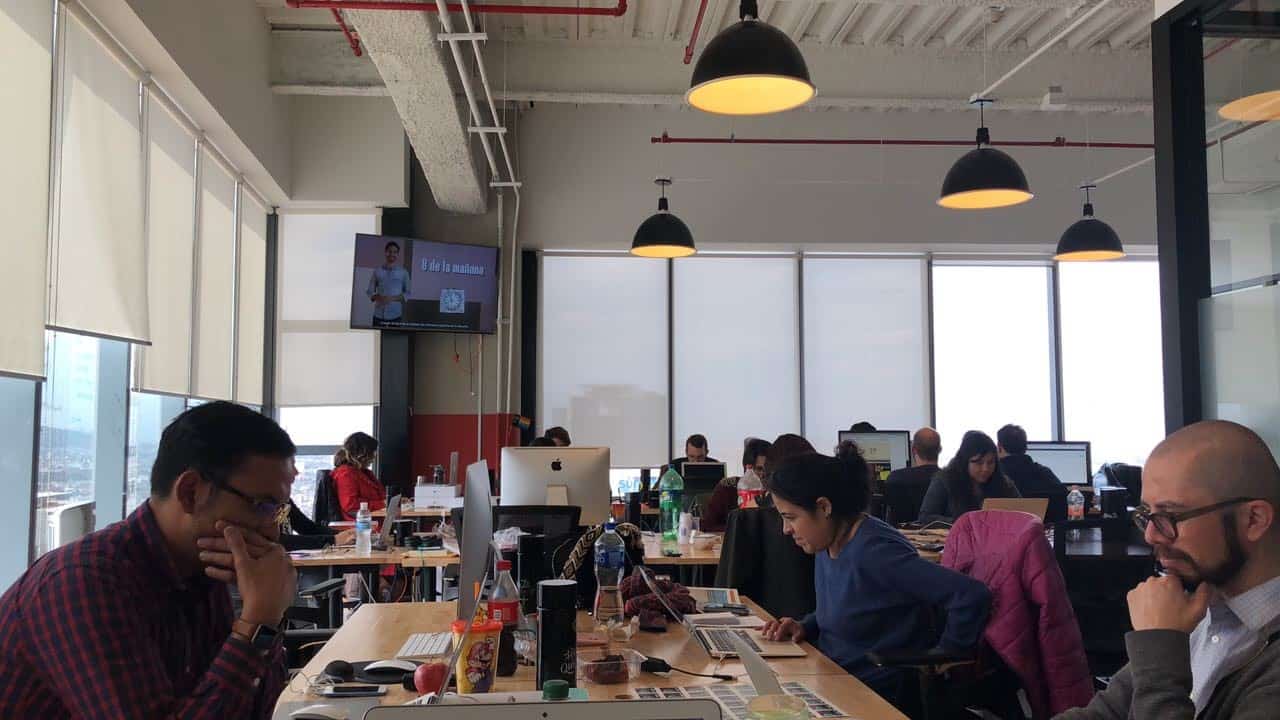 People sit at tables in an open office working on laptop computers
