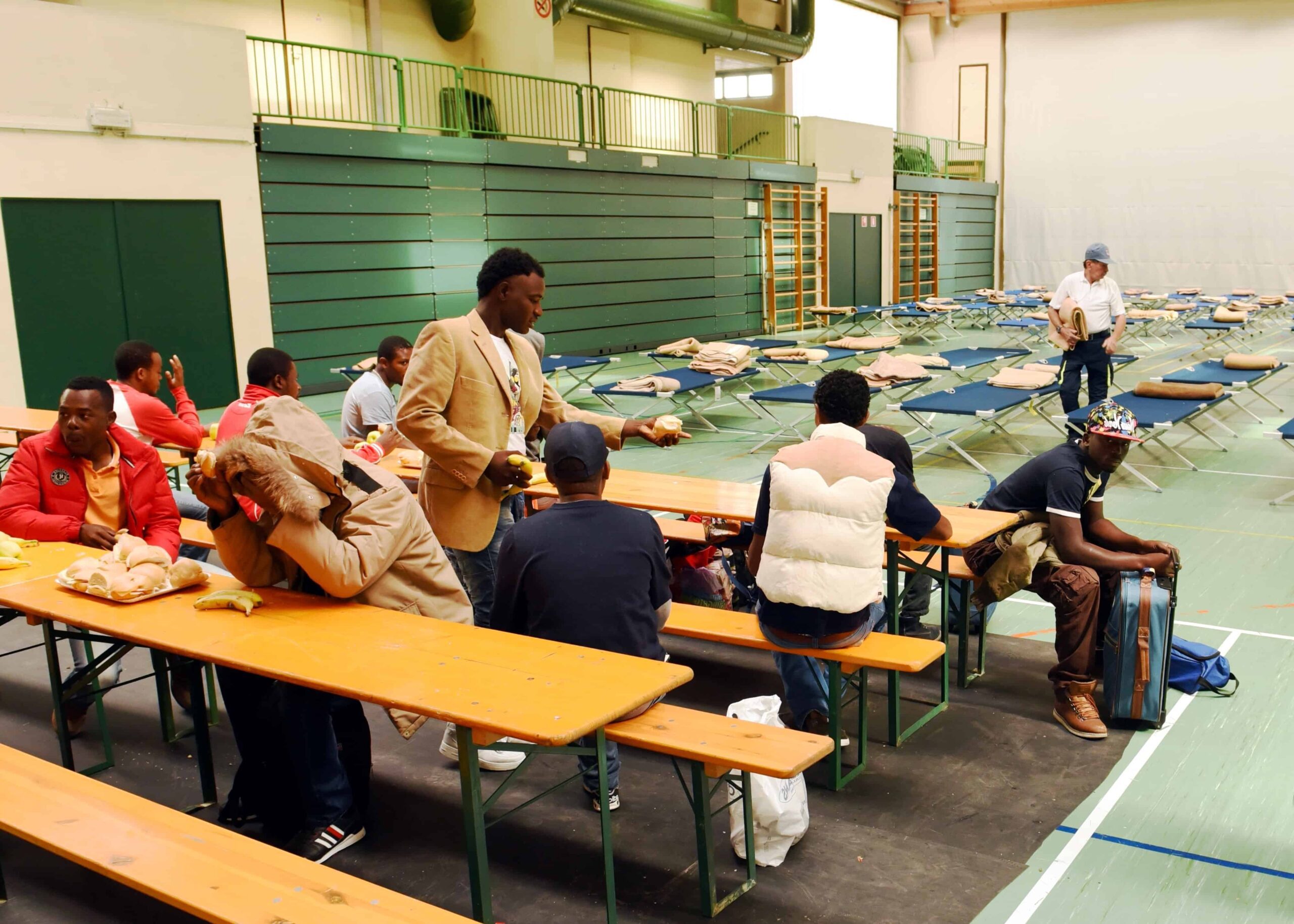 A group of men sit at tables inside a gym.