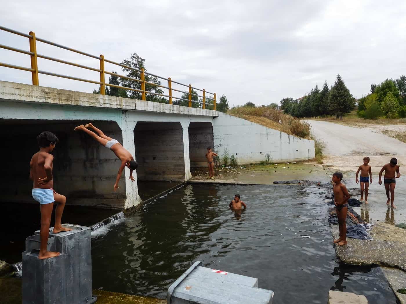 A group of boys swim and dive into the water by a bridge