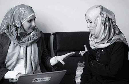 two women in headscarves talking with a laptop