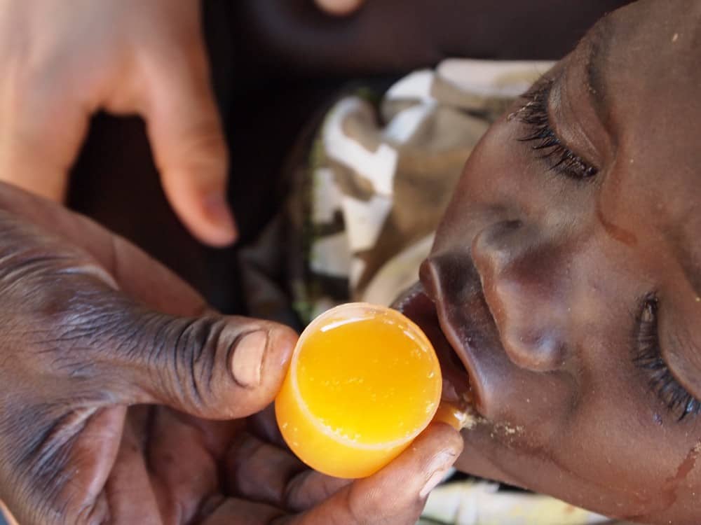 A hand holds a cup of medicine up to a child's mouth