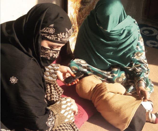 Two Afghan women in burquas sit with a baby on the ground