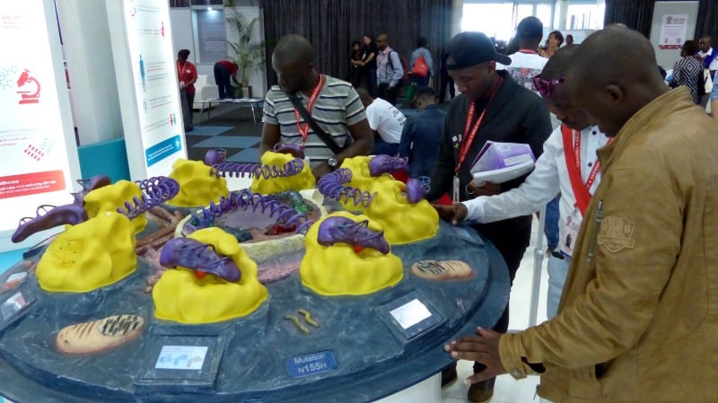 Conference participants stand around a table with a model of a virus on it