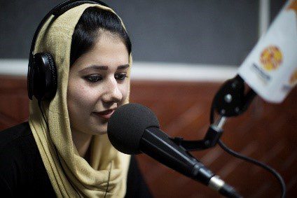 A woman wearing a head scarf sits in front of a microphone