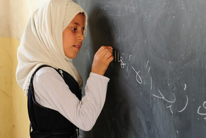 A young girl writes in Arabic on a blackboard.